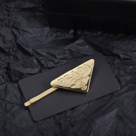 Pinza de pelo dorada con logo de triángulo